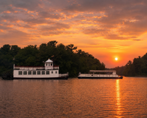 Two boats on a calm river at sunset with trees and a vibrant orange sky in the background.