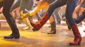 People wearing cowboy boots line dancing on a wooden floor, their legs mid-step in unison.